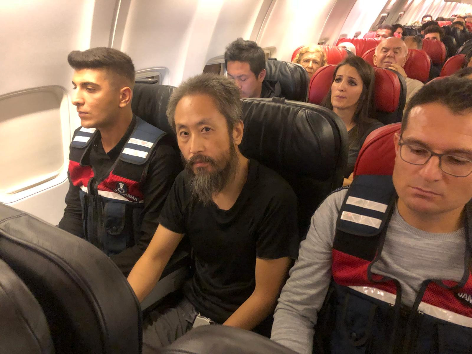 Japanese journalist Jumpei Yasuda sits between two Turkish gendarmes on a Istanbul-bound flight due for departure at Hatay airport