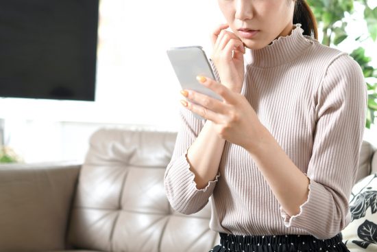 携帯電話（スマートフォン）を持ちながら悩む若い黒髪の女性