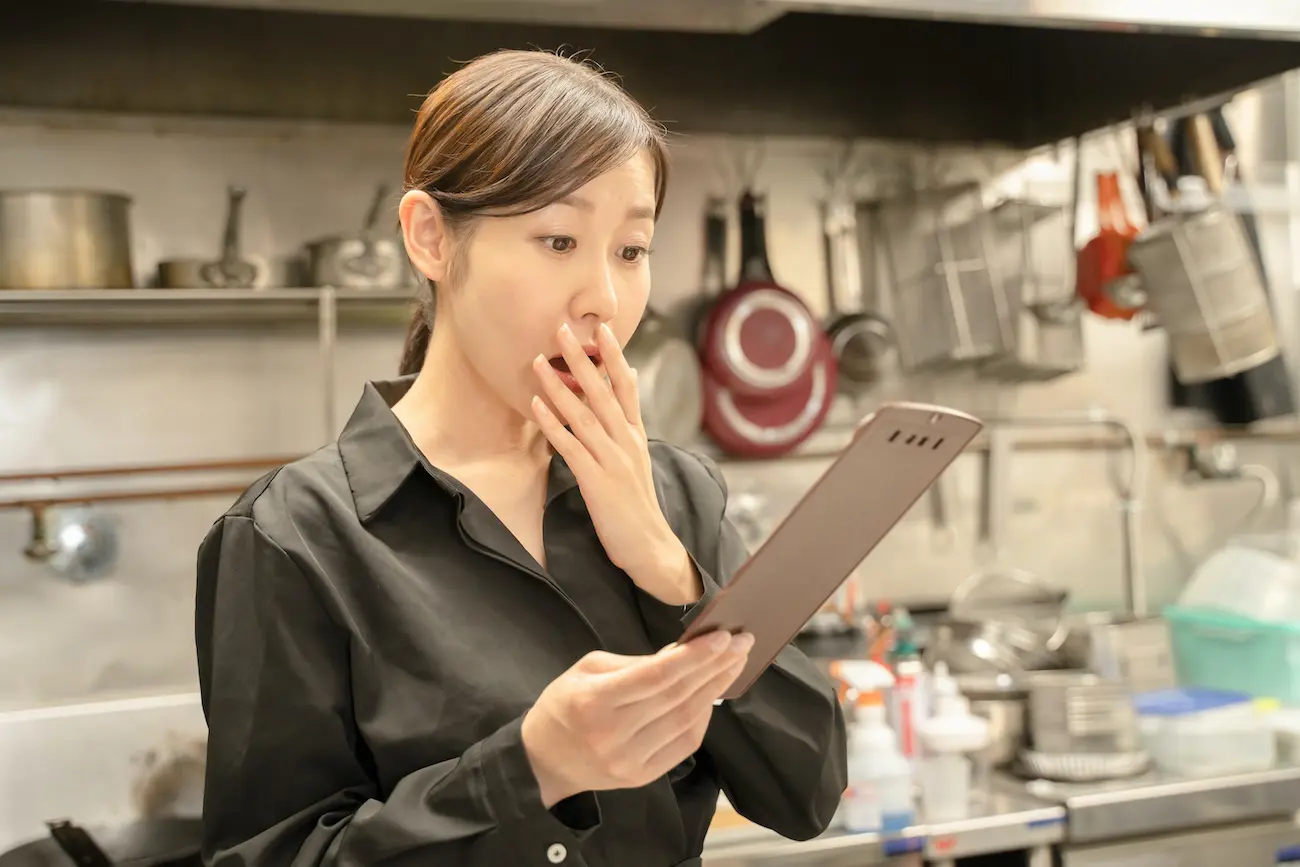 飲食店で伝票確認し驚く女性スタッフ