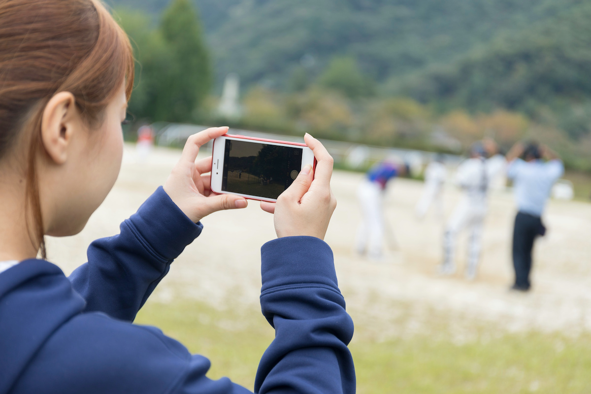 野球の試合をスマホで撮影する野球部マネージャー