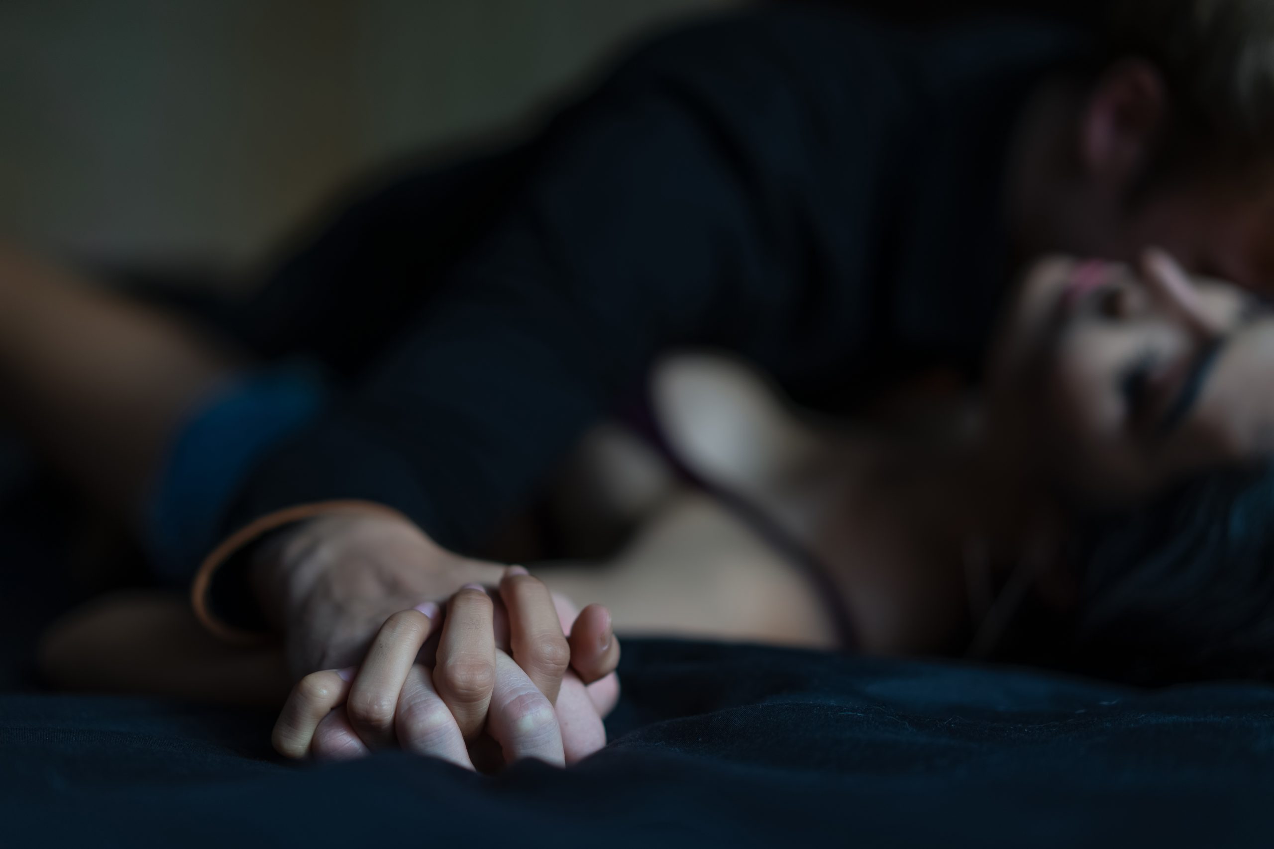 Man's hand holding a woman hand for rape and sexual abuse concept. Couple in love holding hands tight in bed close-up touching each other on a black blanket, enjoying honeymoon, valentine's day